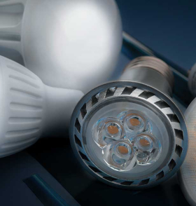 Close-up of assorted LED light bulbs on a dark blue background, highlighting a silver-rimmed spotlight with four visible LED chips in front and white bulbs with clusters of small yellow-orange diodes to the right, with the AVIENT logo in the bottom corner.