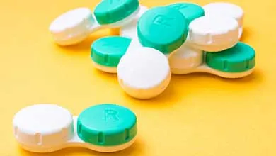 Close-up of multiple contact lens cases, green and white lids, piled on a yellow background.