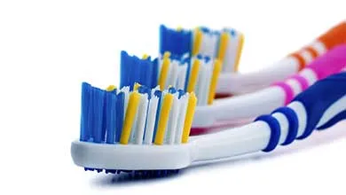 Close-up of colorful toothbrushes, foreground brush has blue, yellow, and white bristles.