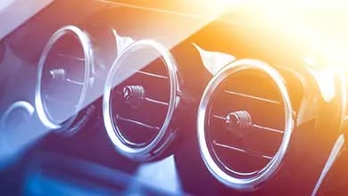 Close-up of three round car air vents with chrome edges, with sunlight flaring in the upper right corner.