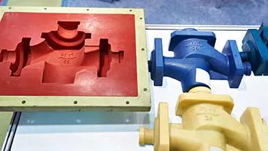 A red industrial valve mold is shown beside a finished blue valve and a finished yellow valve.