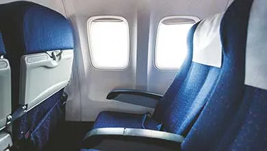 Interior of an airplane cabin showing blue fabric passenger seats with armrests and window light.