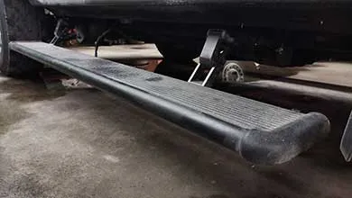 Close-up, low-angle view of a black retractable running board extended from a vehicle’s side.