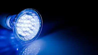 Close-up of a glowing LED bulb emitting bright blue light onto a reflective surface, set against a black background.