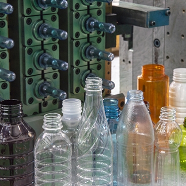 Close-up of PET plastic bottle manufacturing process showing molds and various transparent, colored, and textured plastic bottles.